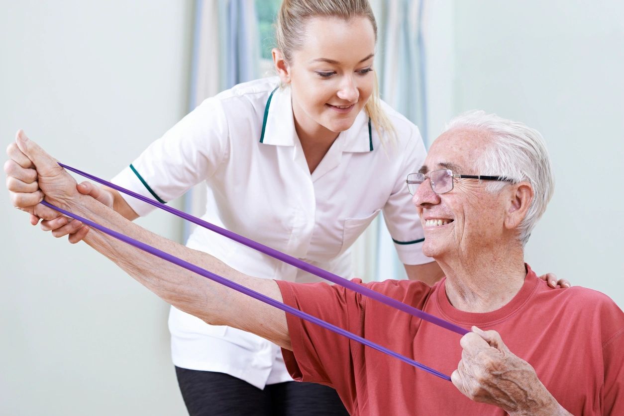 A woman helping an older man exercise with resistance bands.